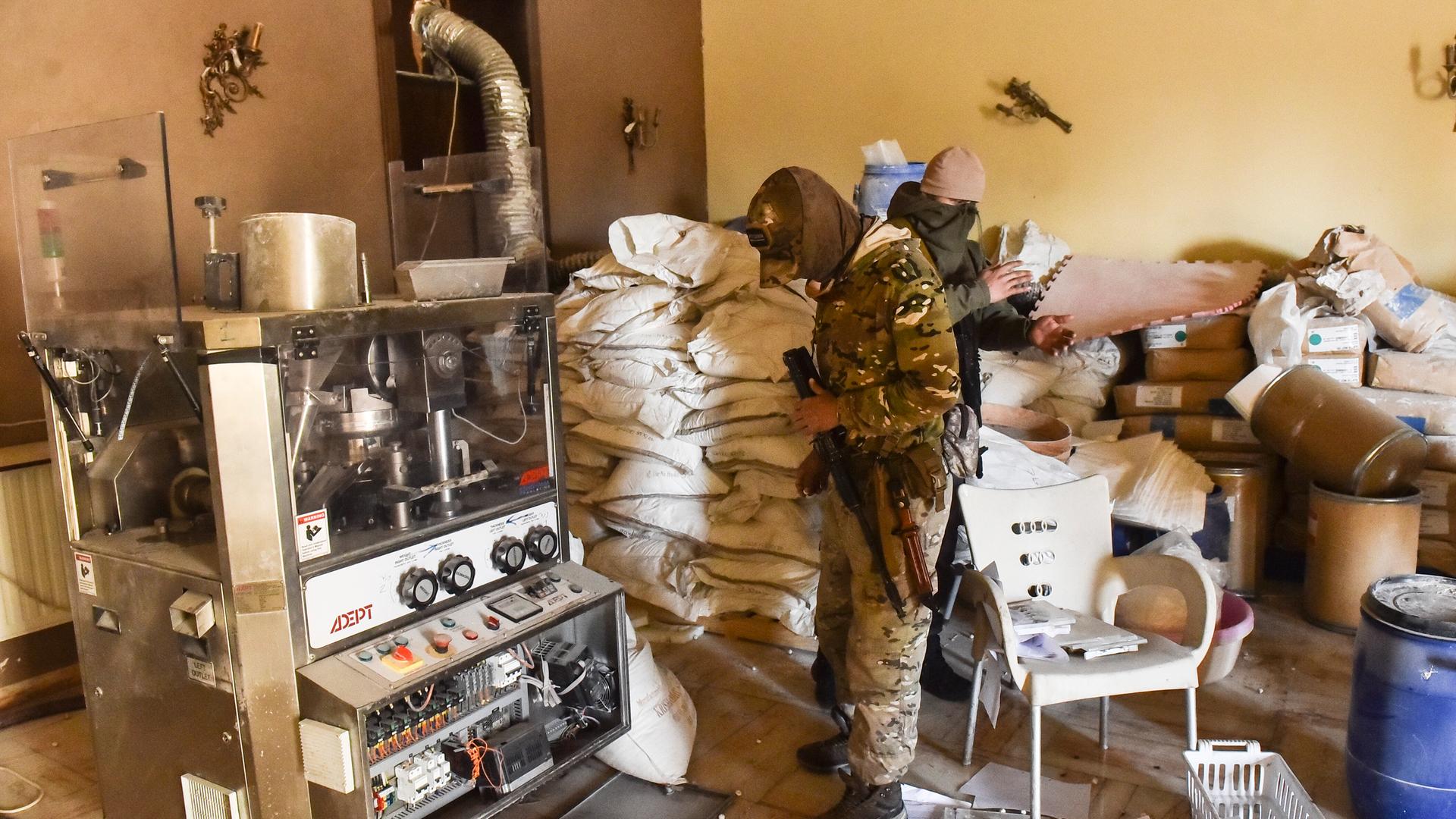 Zwei Personen stehen zwischen Papiersäcken und elektrischem Gerät in einer Drogenproduktionsstätte. 