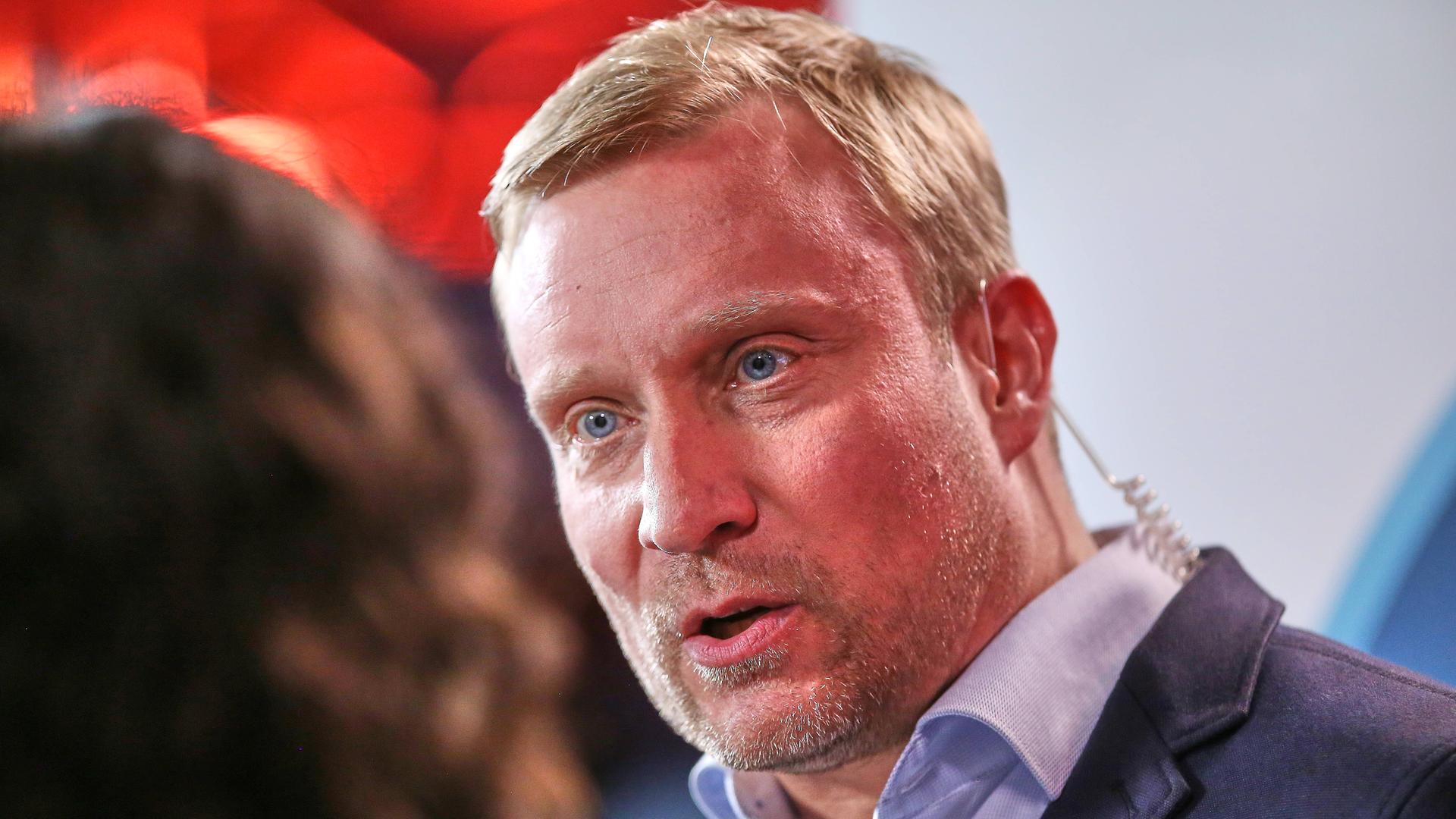 Zu sehen ist der Politikwissenschaftler Benjamin Höhne. Er schaut nach links und spricht mit einer Frau.