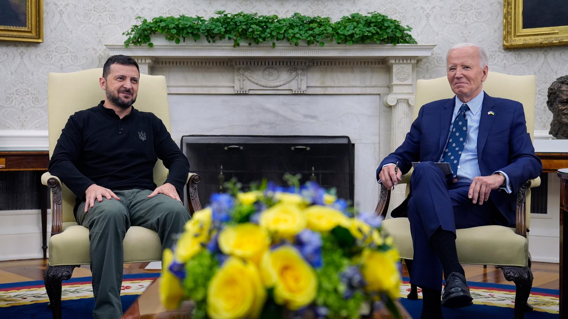 Szene im Weißen Haus in Washington: Der ukrainische Präsident Selenskyj (links) und US-Präsident Joe Biden sitzen neben einem Kamin ein Sesseln, im Vordergrund ist ein Blumengesteck mit gelben und blauen Blumen zu sehen. 