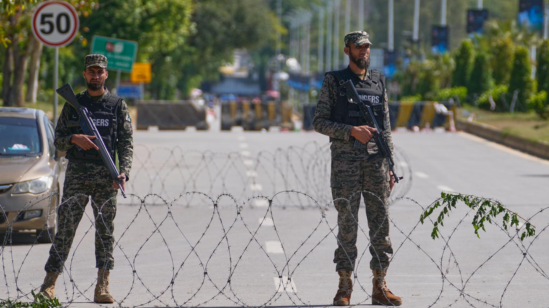 Zwei bewaffnete Soldaten in olivgrünen Unifmormen stehen in islamabad, Pakistan auf einer Straße. Vor ihnen verläuft eine Rolle Stacheldraht quer über die Straße. Zwei bewaffnete Soldaten in olivgrünen Unifmormen stehen in islamabad, Pakistan auf einer Straße. Vor ihnen verläuft eine Rolle Stacheldraht quer über die Straße.