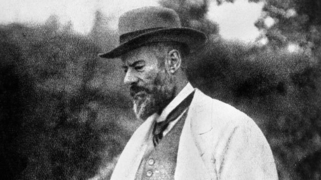Schwarzweißfotografie von Max Weber im Profil. Der Soziologe steht in nachdenklicher Pose in einem Park.