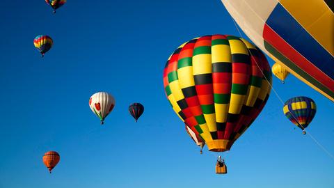 Mehrere bunte Heißlufballons sind vor einem klaren, hellblauen Himmel zu sehen.