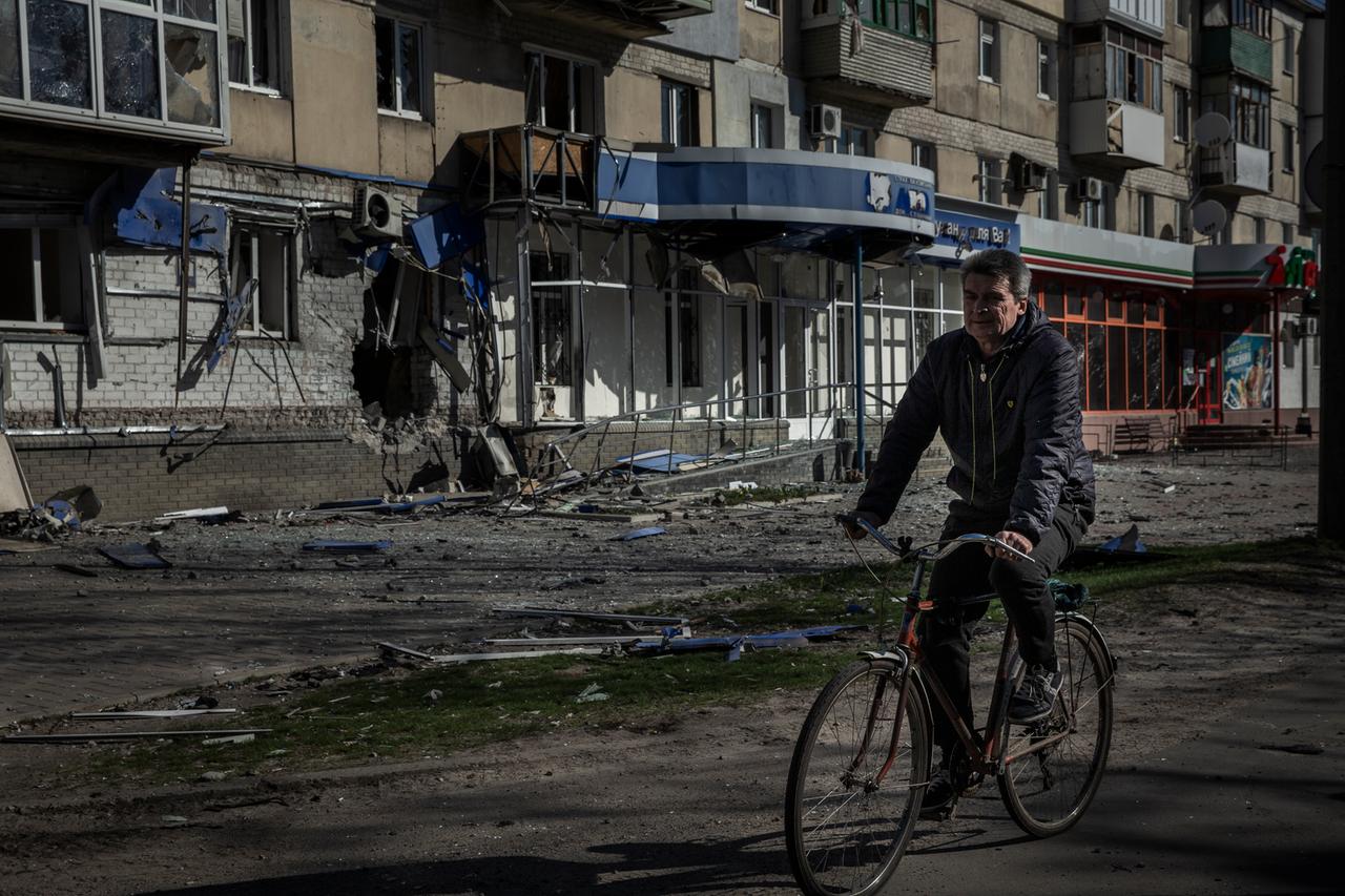 Sjewjerodonezk: Ein Mann fährt mit einem Fahrrad an einem Wohnhaus vorbei, das durch einen früheren russischen Angriff beschädigt wurde.