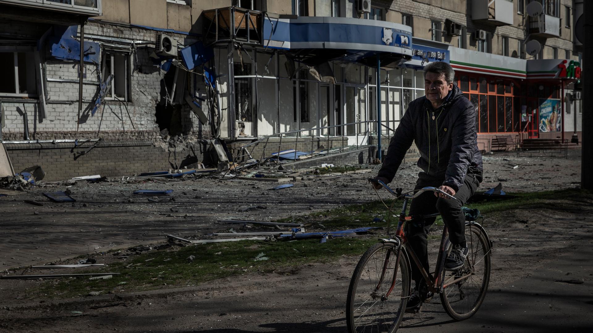 Sjewjerodonezk: Ein Mann fährt mit einem Fahrrad an einem Wohnhaus vorbei, das durch einen früheren russischen Angriff beschädigt wurde.