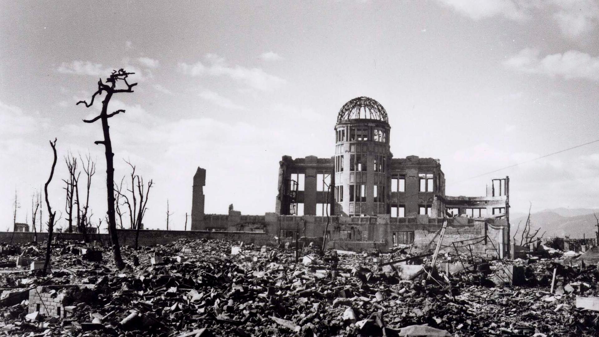 Historische Aufnahme des heute als Friedensdenkmal bekannten Gebäudes in Hiroshima, dessen Ruine nach dem Bombenwurf 1945 aus dem Schutt ragt.  
