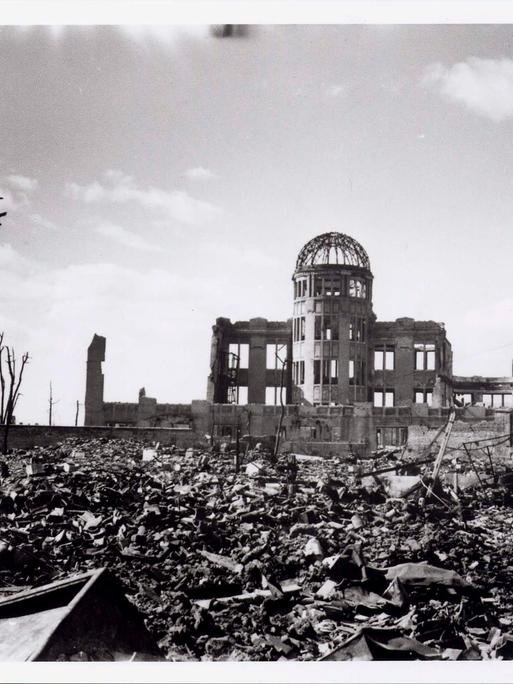 Historische Aufnahme des heute als Friedensdenkmal bekannten Gebäudes in Hiroshima, dessen Ruine nach dem Bombenwurf 1945 aus dem Schutt ragt.  