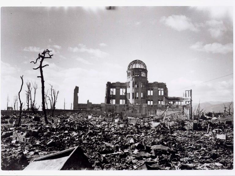Historische Aufnahme des heute als Friedensdenkmal bekannten Gebäudes in Hiroshima, dessen Ruine nach dem Bombenwurf 1945 aus dem Schutt ragt.  