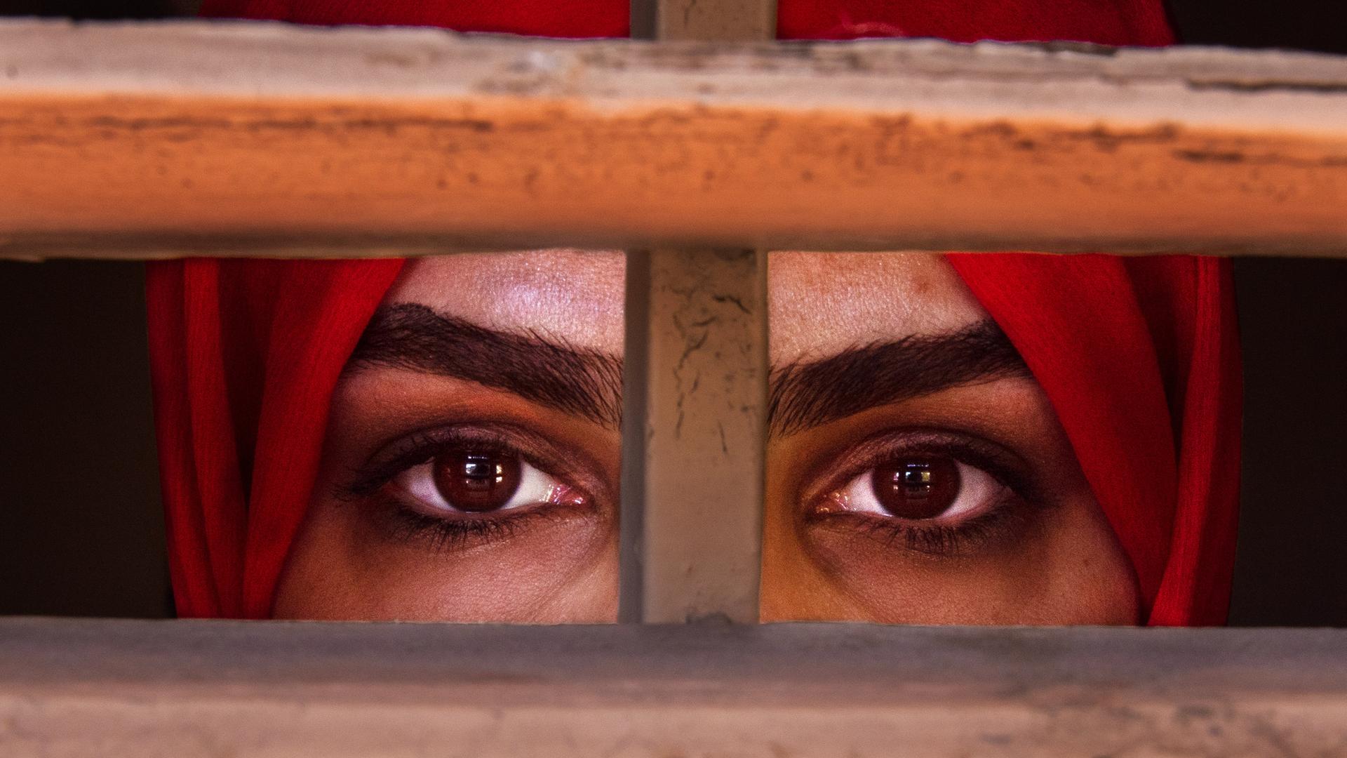 Eine afghanische Frau blickt durch ein vergittertes Fenster 