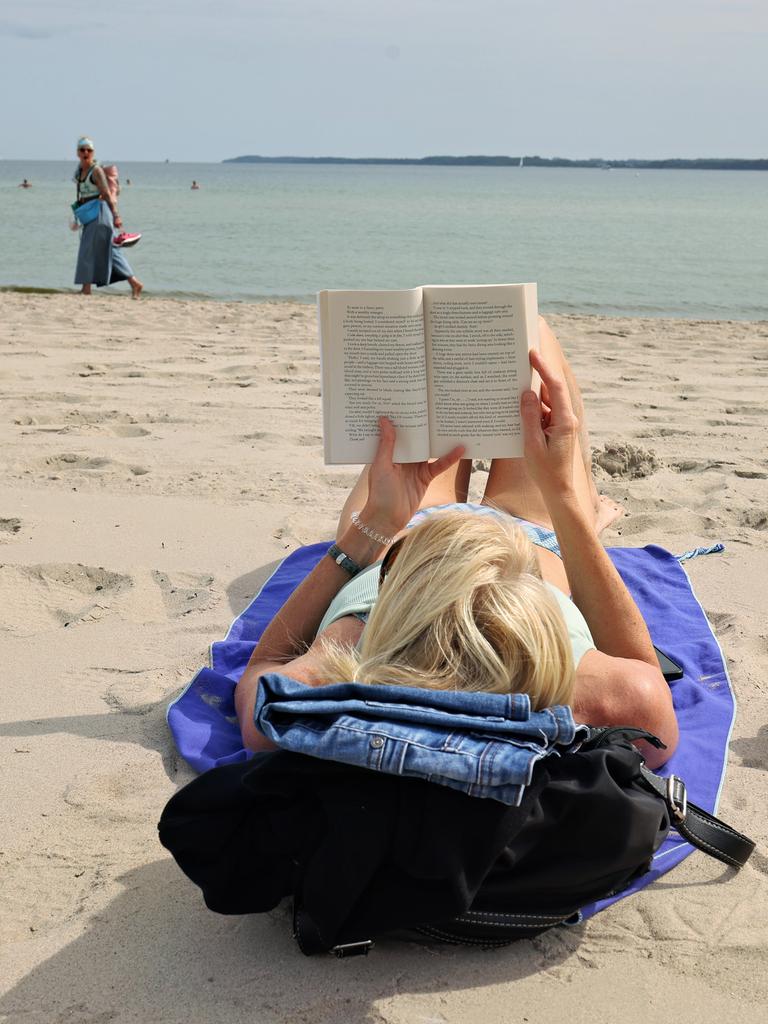 Eine Urlauberin liest an einem Badestrand an der Ostsee ein Buch.