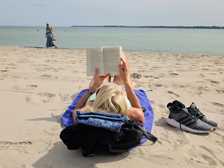 Eine Urlauberin liest an einem Badestrand an der Ostsee ein Buch.