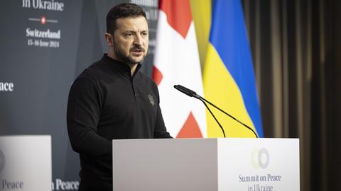 Der ukrainische Präsident Selenskyj steht am Rednerpult, im Hintergrund zu sehen die Flaggen der Schweiz und der Ukraine.