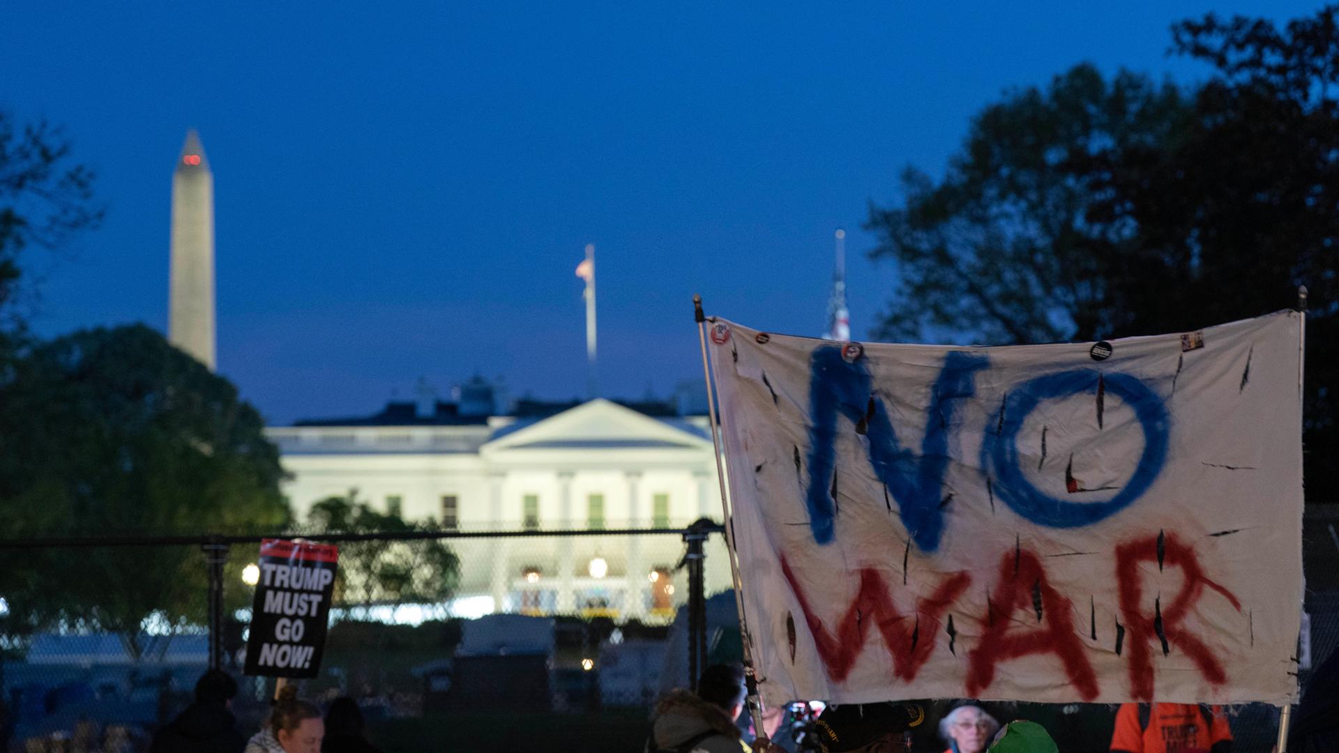 Aktivisten halten ein Transparent mit den Worten "No War" in die Höhe, im Hintergrund ist das Weiße Haus zu sehen