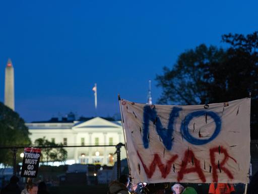 Aktivisten halten ein Transparent mit den Worten "No War" in die Höhe, im Hintergrund ist das Weiße Haus zu sehen