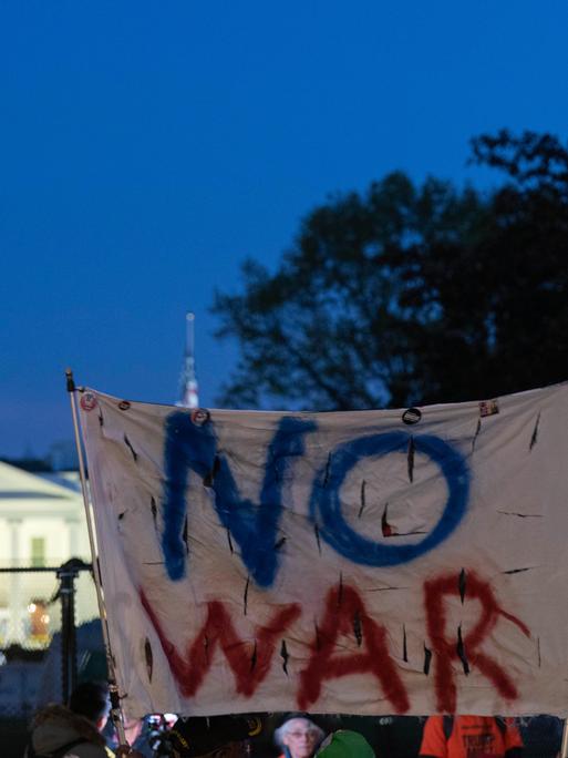 Aktivisten halten ein Transparent mit den Worten "No War" in die Höhe, im Hintergrund ist das Weiße Haus zu sehen