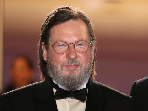 Der Regisseur Lars von Trier mit Brille, Bart und längeren Haaren trägt eine Fliege, weißes Hemd und Jackett.