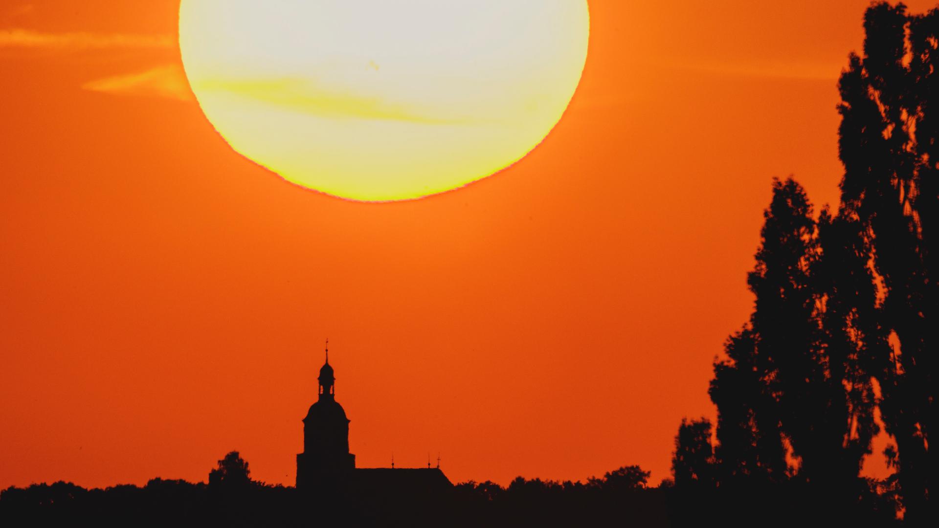 Eine Kirche zeichnet sich am 26.06.2026 vor der untergehenden Sonne in Malschwitz ab. 