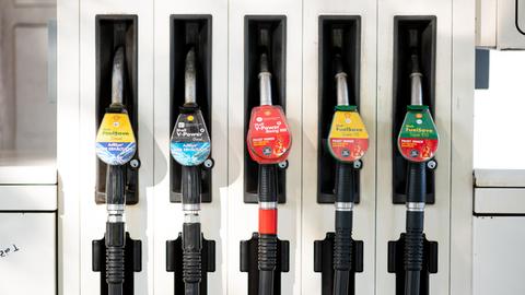 Zapfpistolen für verschiedene Kraftstoffe stecken in einer Zapfsäule an einer Tankstelle.