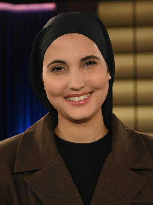 Comedienne Anissa Loucif zu Gast in der WDR Talkshow Kölner Treff. Sie trägt ein dunkles Kopftuch und lacht vergnügt in die Kamera. 