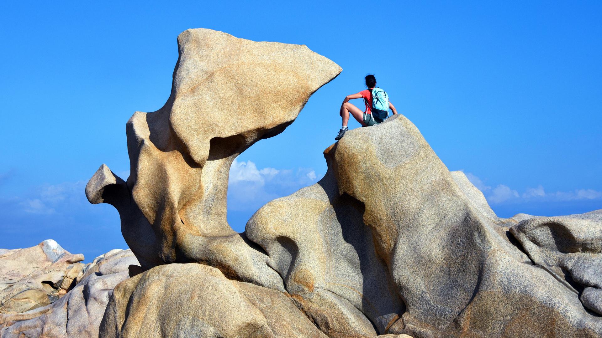 Eine junge Wanderin macht Pause an charakteristischen Kuestenfelsen bei Campomoro, Frankreich, Korsika.
