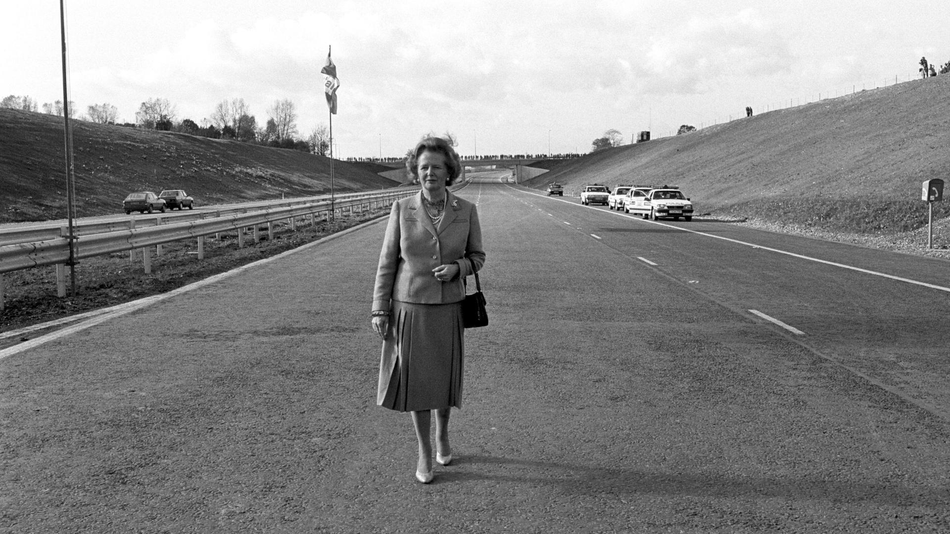 Ein Scharz-Weiß-Foto zeigt die damalige britische Premierministerin Margaret Thatcher nach der offiziellen Eröffnung der Autobahn M25 in Hertfordshire allein auf der Fahrbahn stehend.