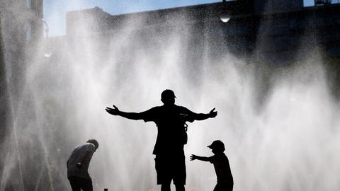 Passanten erfrischen sich an Wasserfontänen, die von der Stadt Köln im Rahmen der Hitzeaktion 'Cooling Cologne' auf dem Rudolfplatz ausgelegt wurden. 