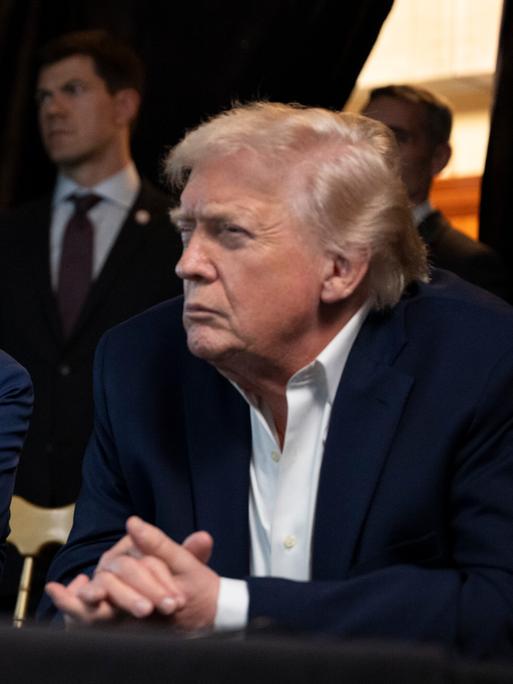 Donald Trump beobachtet mit grimmiger Mine an einem Tisch sitzend von Mar-a-Lago aus die Übertragung des Angriffs in Caracas.
