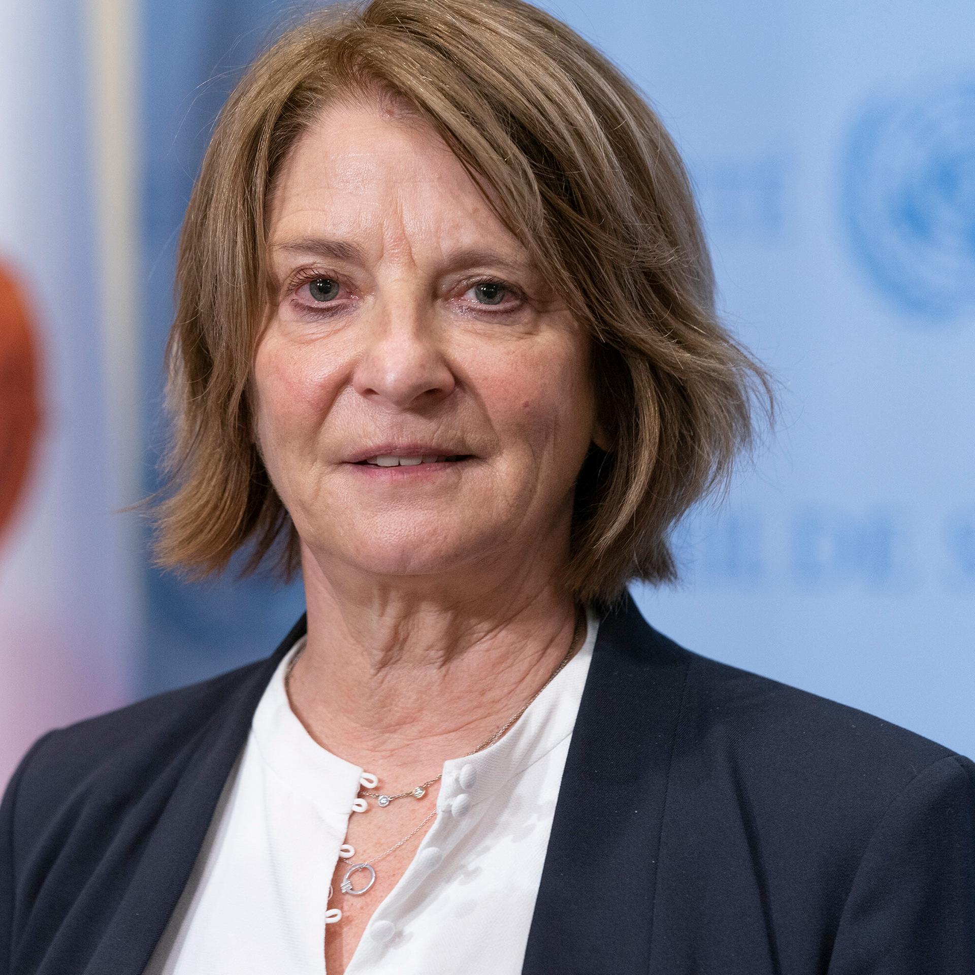 Juul mit mittellangen braunen Haaren blickt leicht lächelnd in die Kamera. Links von ihr ein Mikrofon, dahinter unscharf eine blaue Wand.  