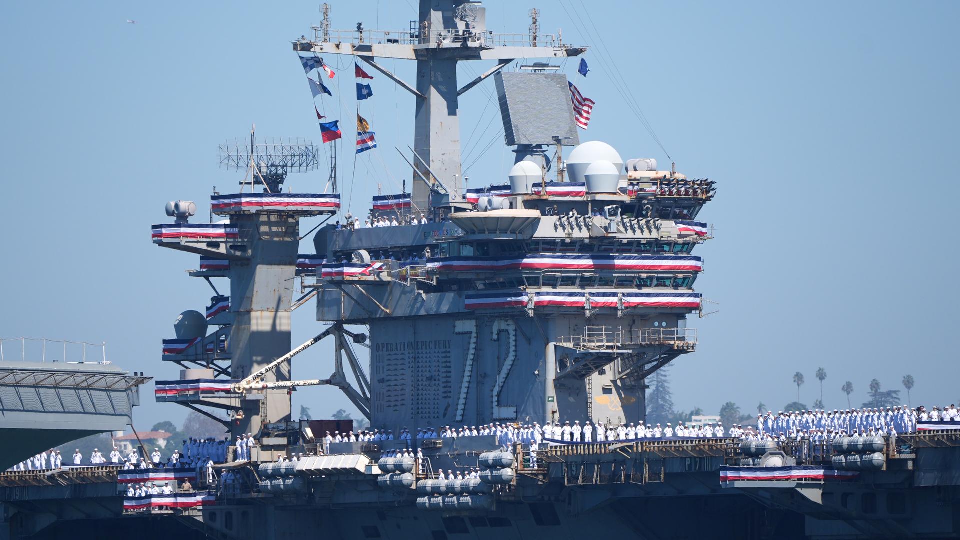 Der Flugzeugträger USS Abraham Lincoln. An Deck stehen Matrosen. Flaggen der USA sind gehisst.