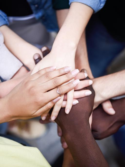 Junge Menschen strecken ihre Arme aus. Die Hände treffen sich in der Mitte des Kreises, den ihre Körper - außerhalb des Bildes - bilden.