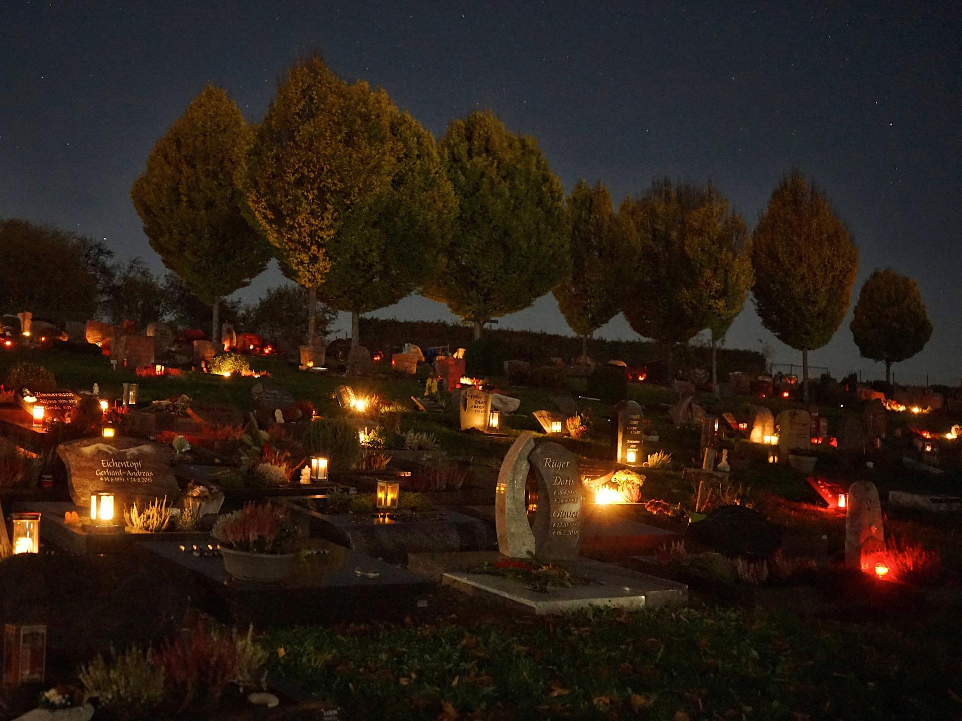 Wir sehen einen Friedhof bei Nacht, der von Grablichtern erleuchtet ist. 