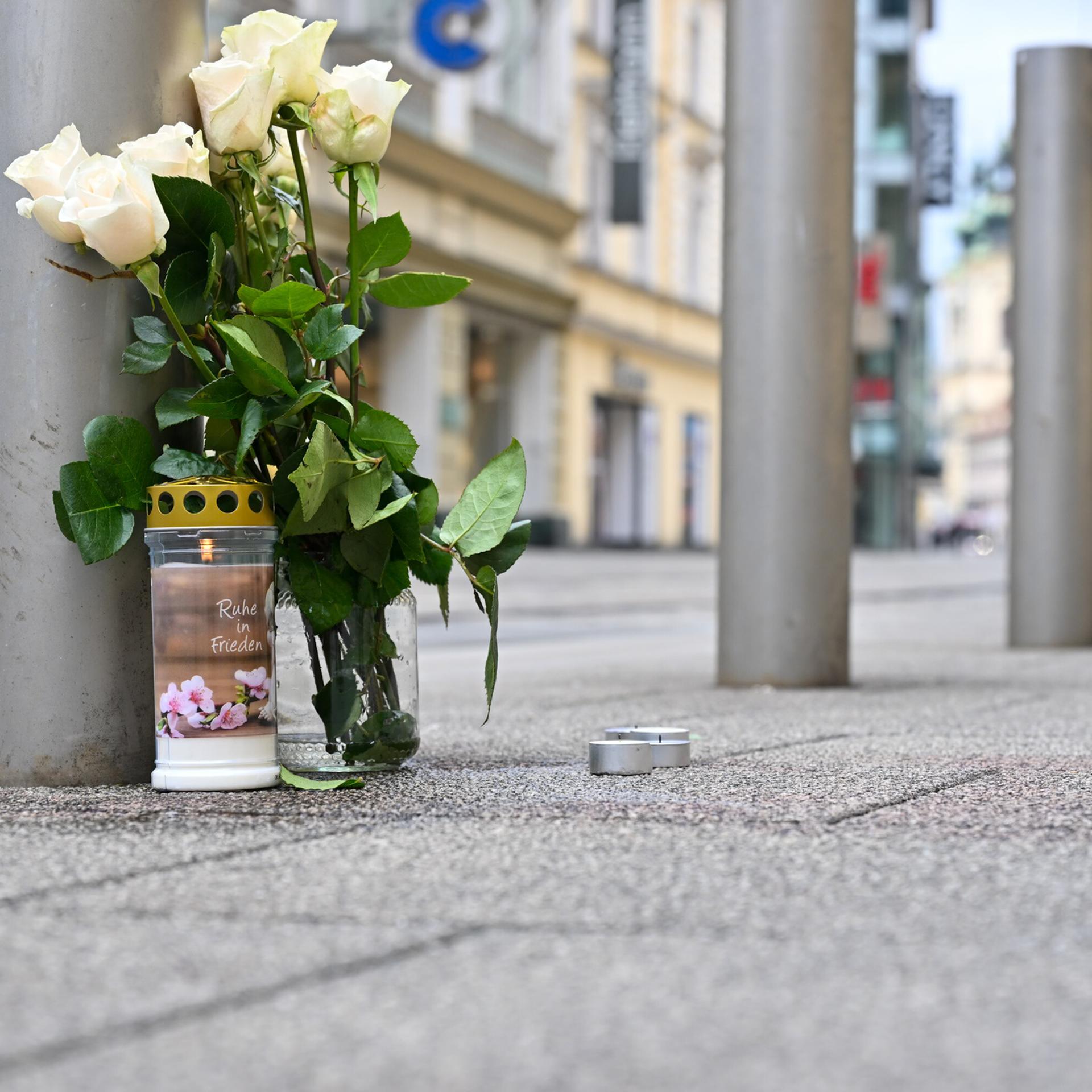 Blumen und eine Kerze stehen in der Nähe des Tatorts nach einem tödlichen Messerangriff in der Linzer Innenstadt.
