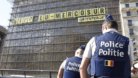 An einem Gebäude hängt ein langes gelbes Schild. Darauf steht in schwarzen Großbuchstaben: „Stop EU-Mercusor“. Darunter steht in kleinerer Schrift das Wort „Greenpeace“. 