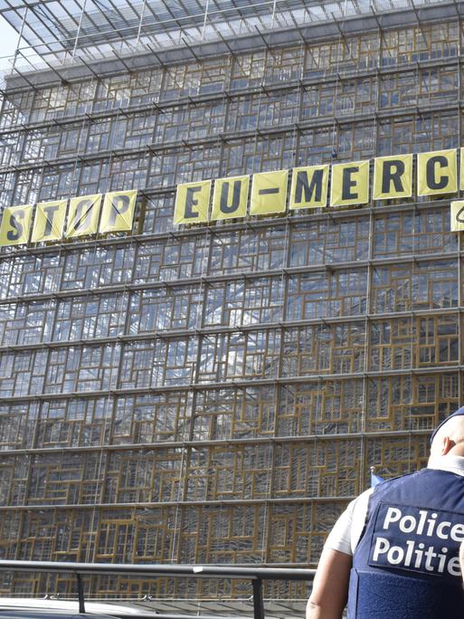 An einem Gebäude hängt ein langes gelbes Schild. Darauf steht in schwarzen Großbuchstaben: „Stop EU-Mercusor“. Darunter steht in kleinerer Schrift das Wort „Greenpeace“. 
