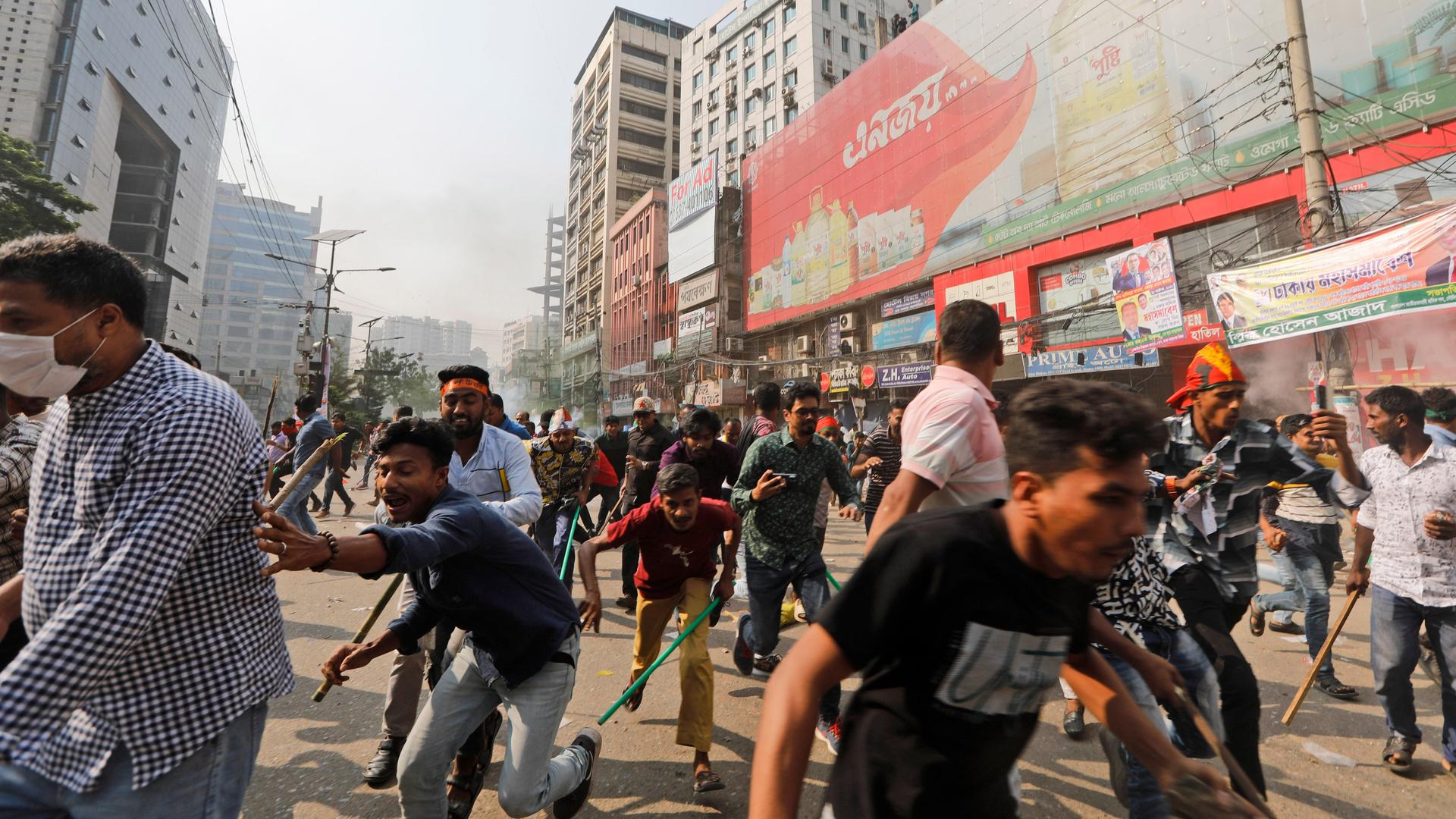 Menschen rennen auf einer Straße in Panik auseinander. Im Hintergrund ist Rauch zu sehen.