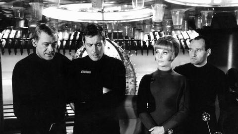 Claus Holm, Dietmar Schönherr, Eva Pflug und Friedrich G Beckhaus stehen in futuristischer Kleidung in einem Science-Fiction-Set wie es für die Sechzigerjahre typisch