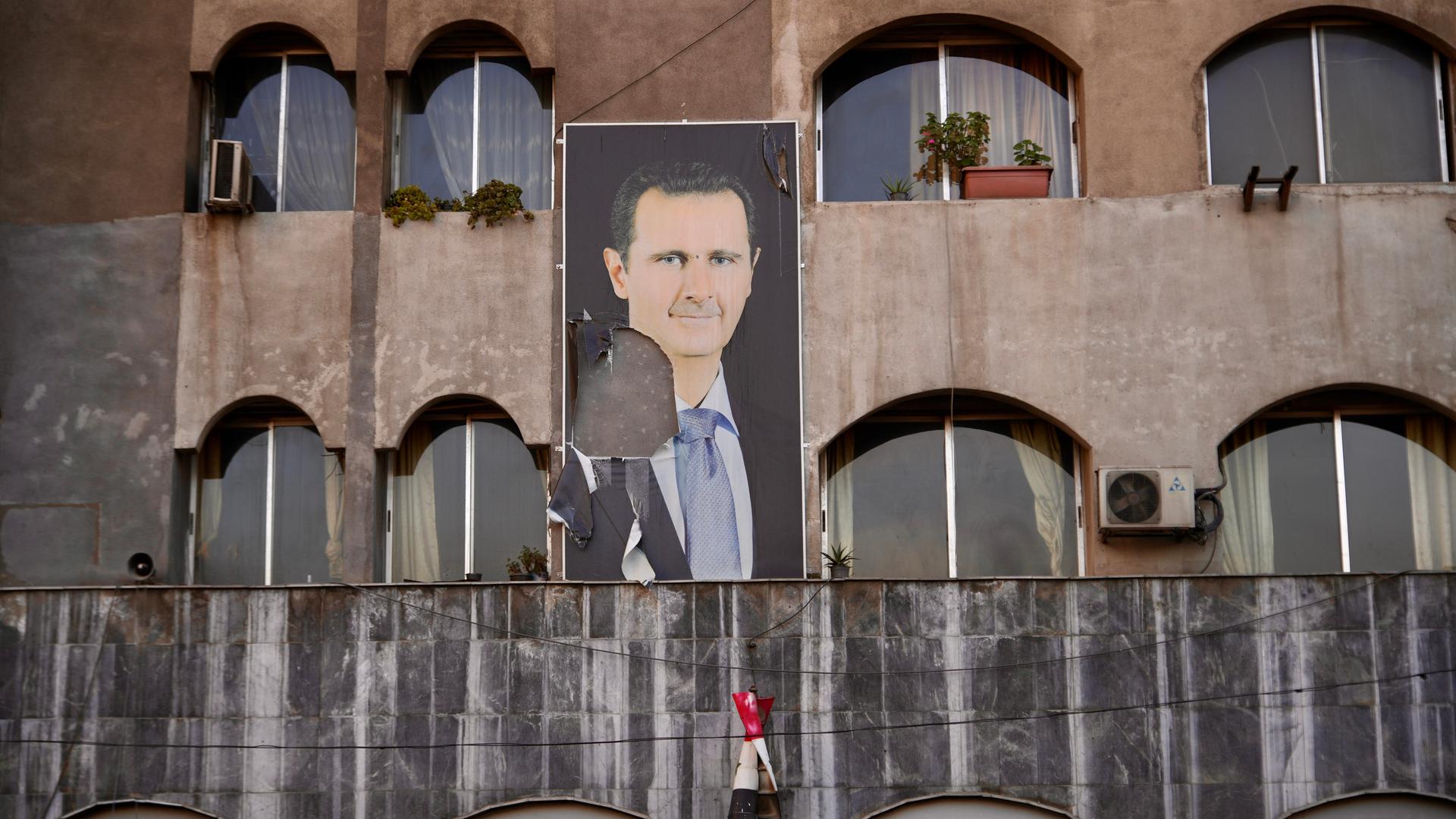 An einer Wand in Damaskus hängt ein Plakat des früheren Machthabers Baschar Al-Assad, von dem ein Teil abgerissen wurde.