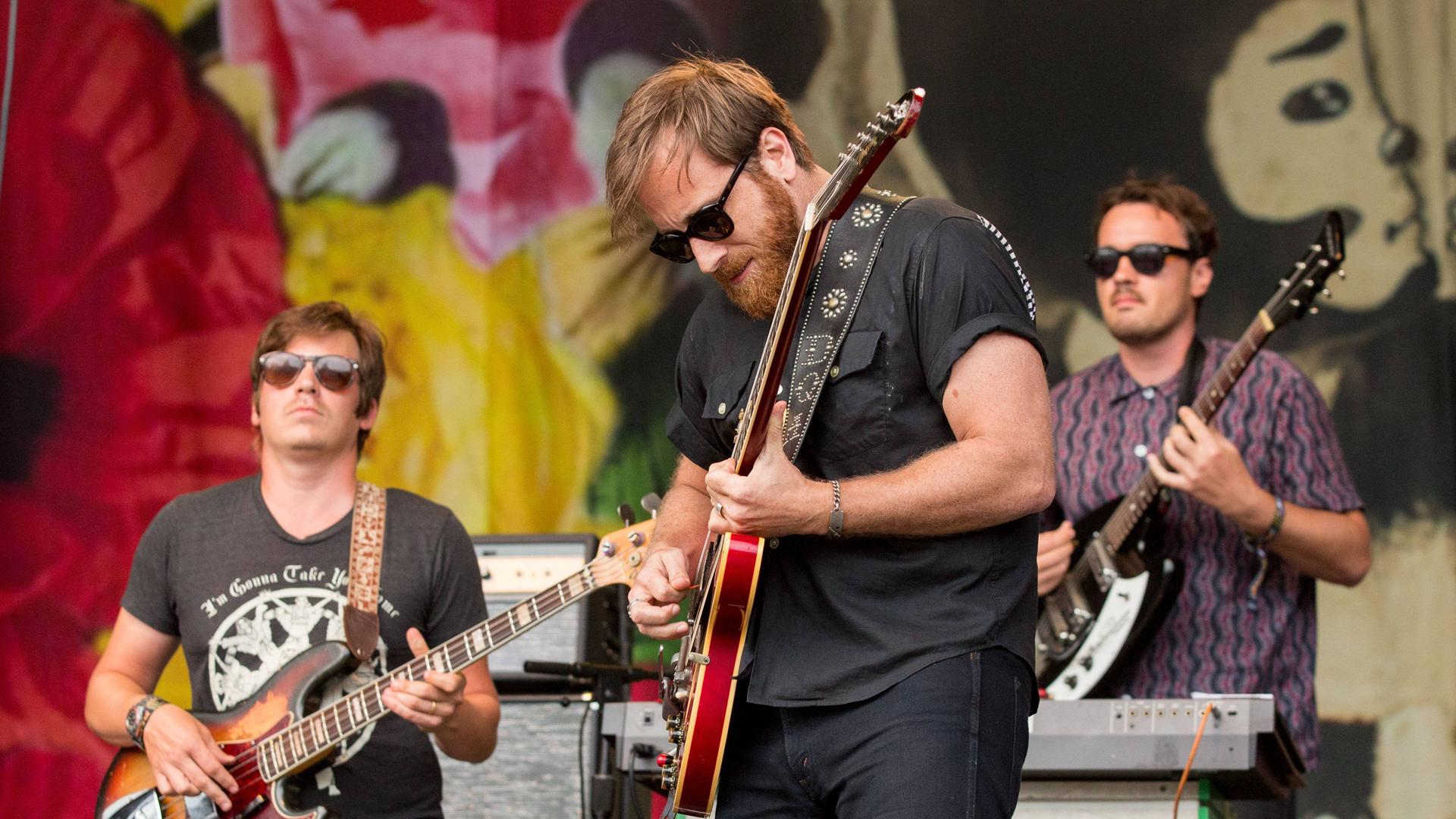 Der Gitarrist Dan Auerbach steht mit Gitarre und seiner Band "The Arcs" auf einer Bühne Der Gitarrist Dan Auerbach steht mit Gitarre und seiner Band "The Arcs" auf einer Bühne