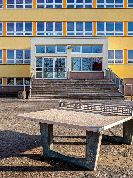 Leerer Schulhof mit Schulgebäude mit Tischtennisplatte im Vordergrund