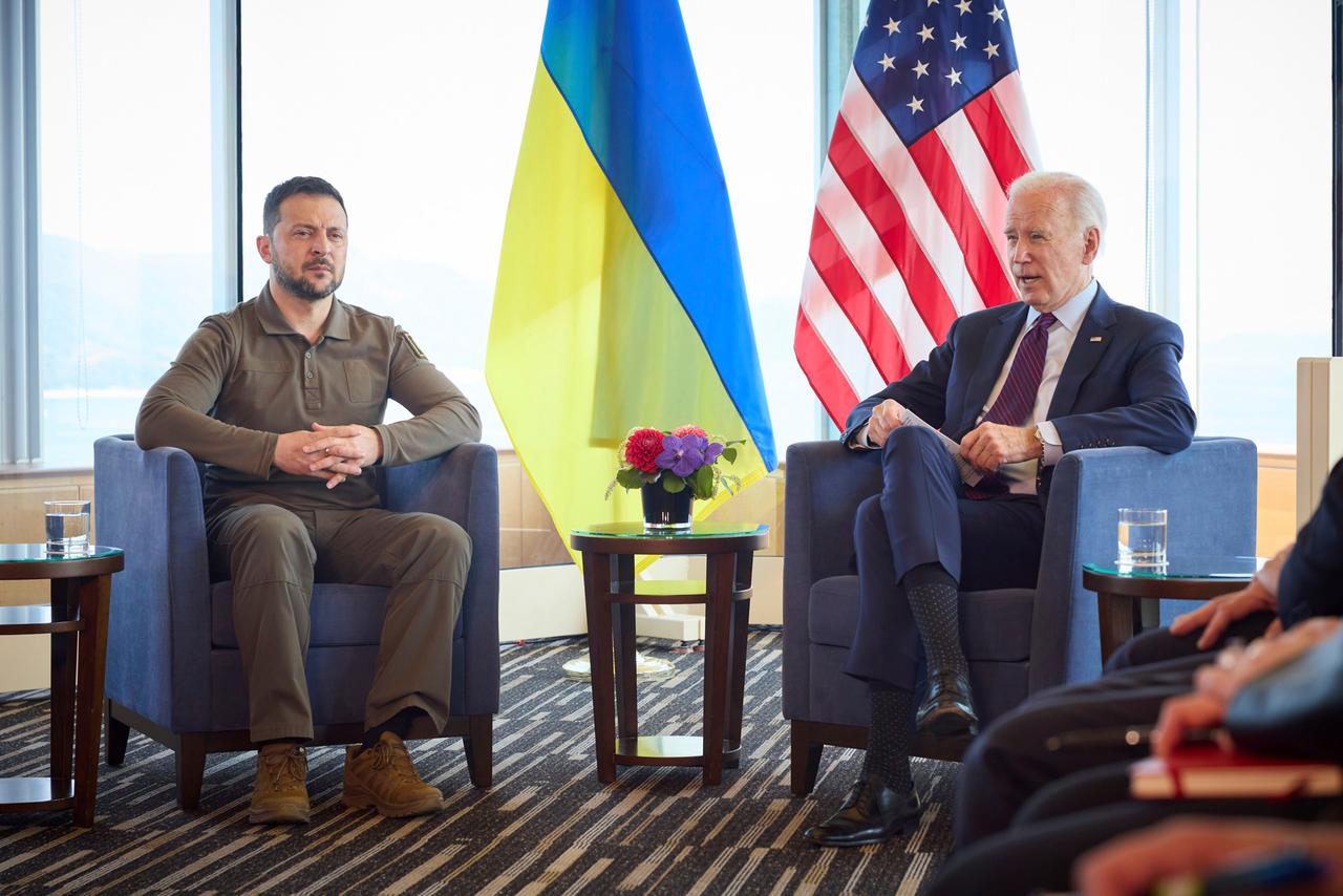 Jüngerer Mann in Armeekleidung und alter Mann in Zivil sitzen vor der ukrainischen und der US-Flagge