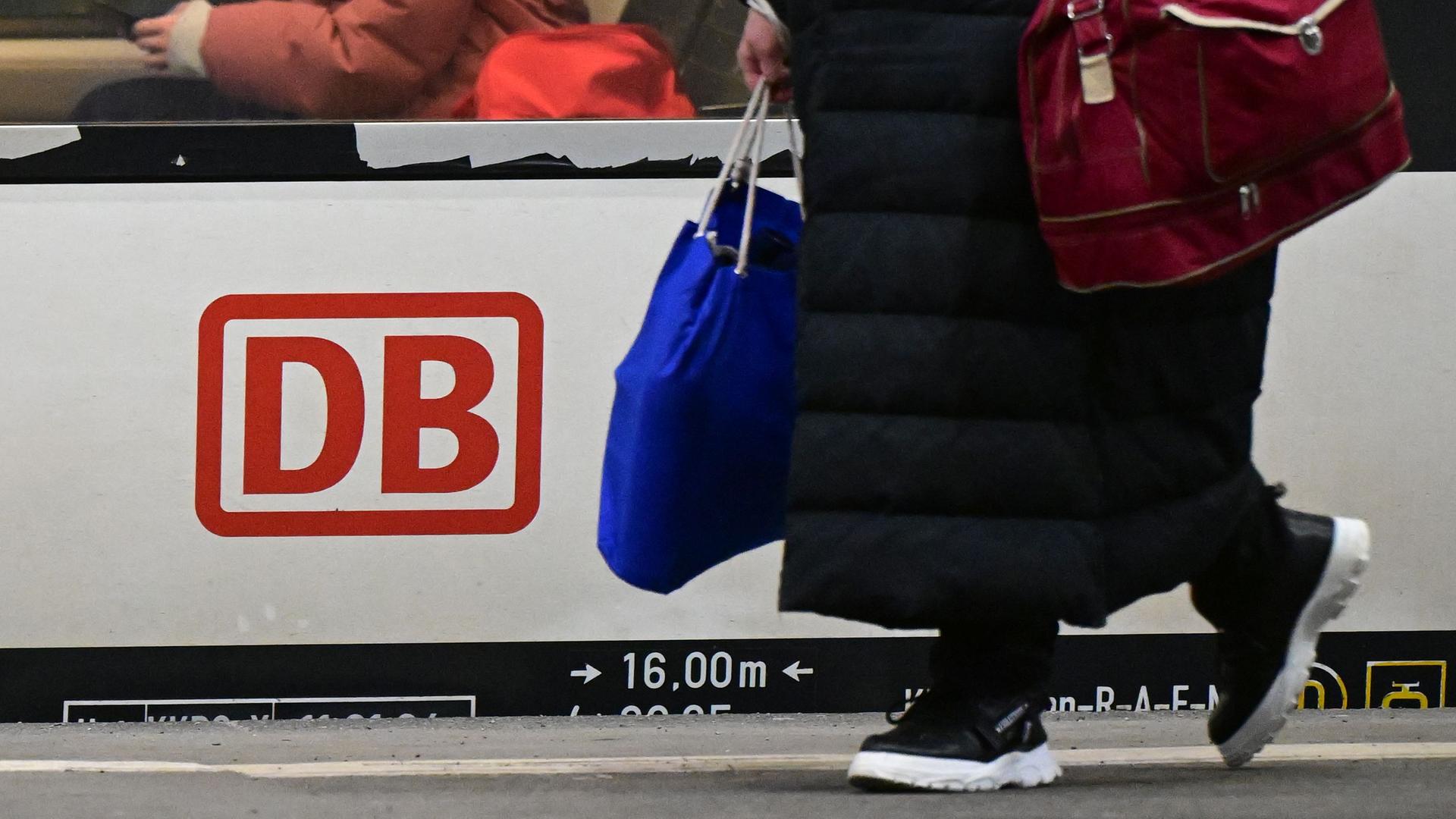 Ein Regionalzug mit dem Logo der Deutschen Bahn steht im Hauptbahnhof zur Abfahrt bereit. Eine Frau geht mit Taschen in der Hand daran vorbei. Ein Regionalzug mit dem Logo der Deutschen Bahn steht im Hauptbahnhof zur Abfahrt bereit. Eine Frau geht mit Taschen in der Hand daran vorbei.