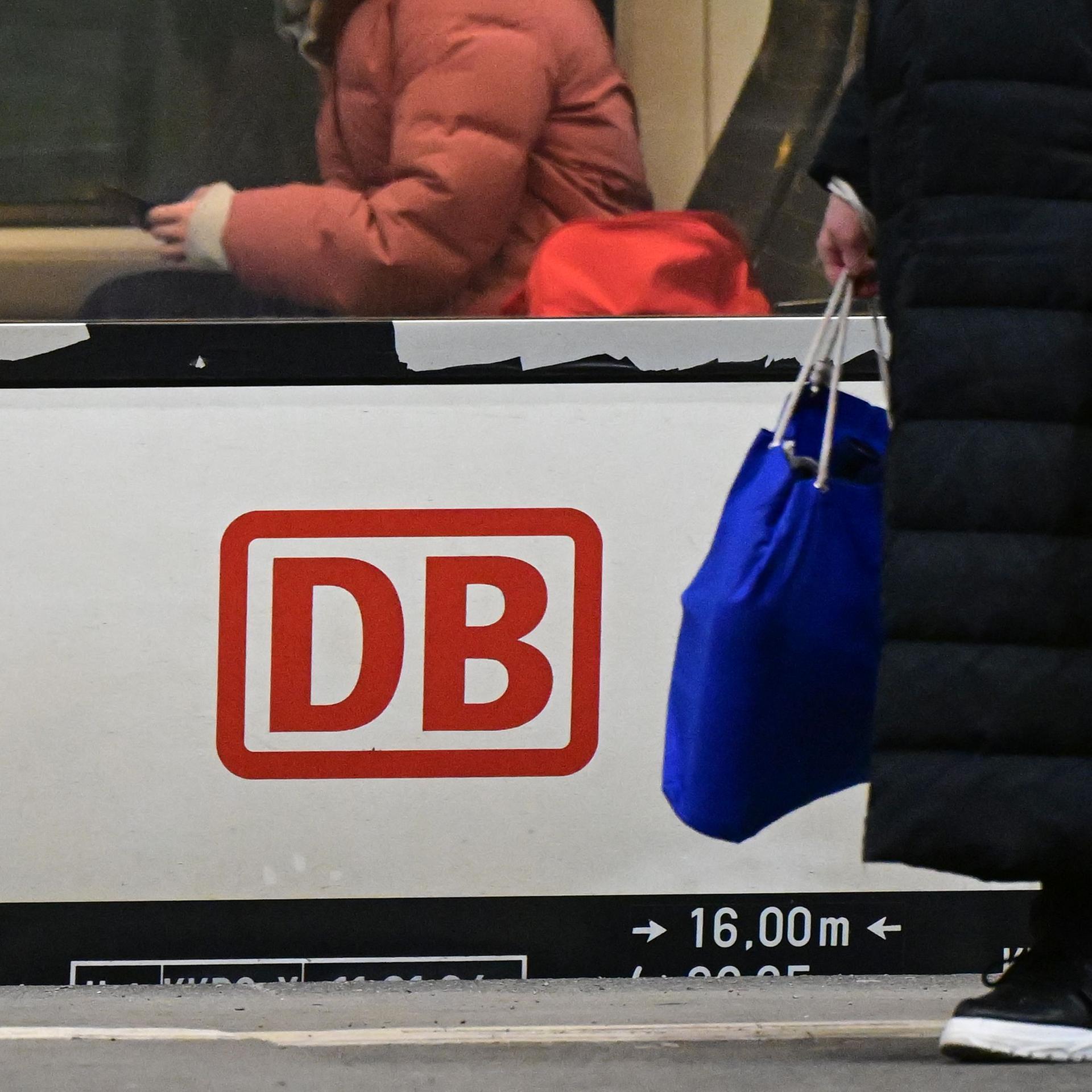 Ein Regionalzug mit dem Logo der Deutschen Bahn steht im Hauptbahnhof zur Abfahrt bereit. Eine Frau geht mit Taschen in der Hand daran vorbei. 