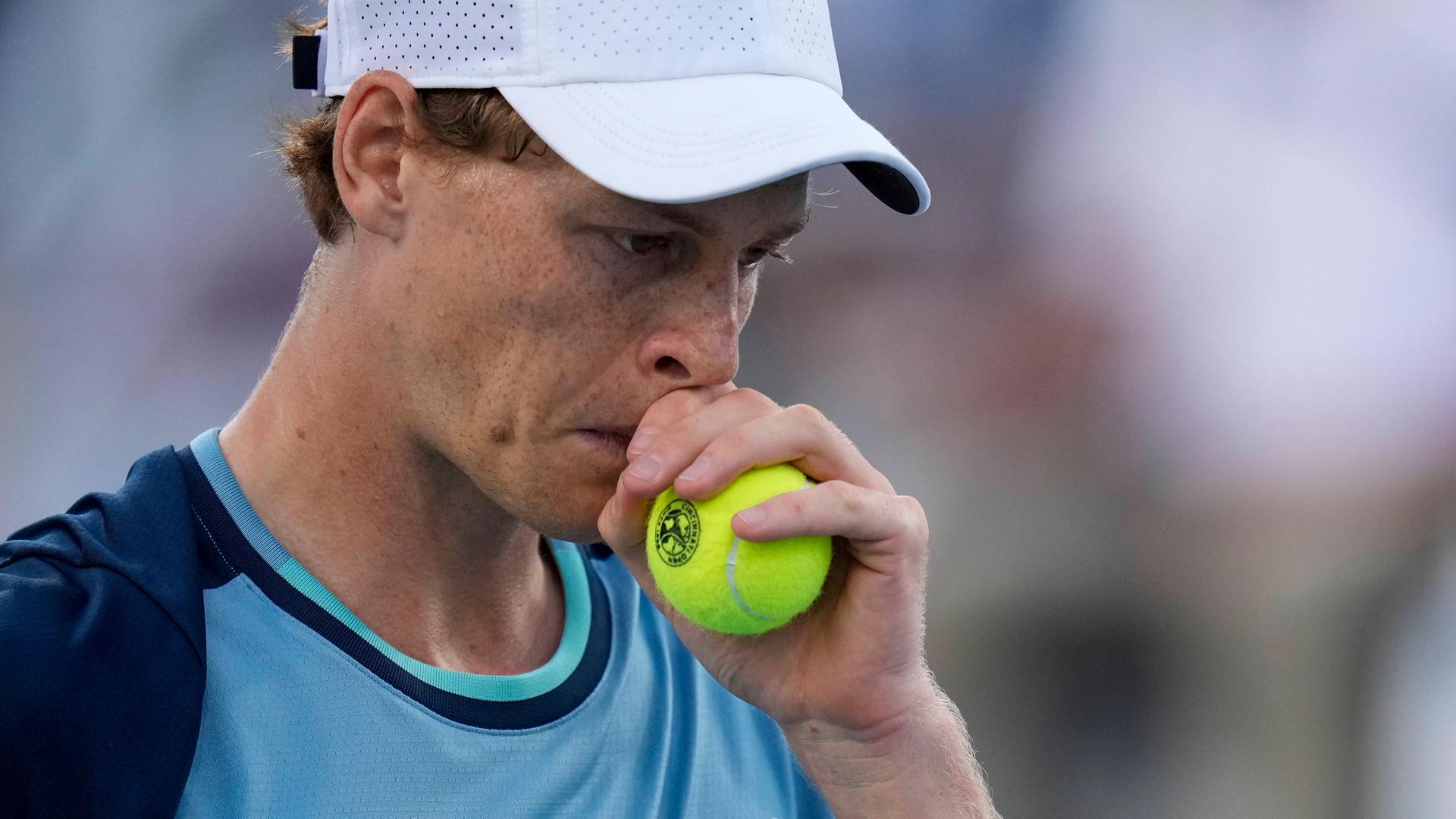 Tennis-Spieler Jannik Sinner in einer Porträt-Aufnahme hält sich einen Tennisball während eines Turnierspiels nachdenkend ans Gesicht.