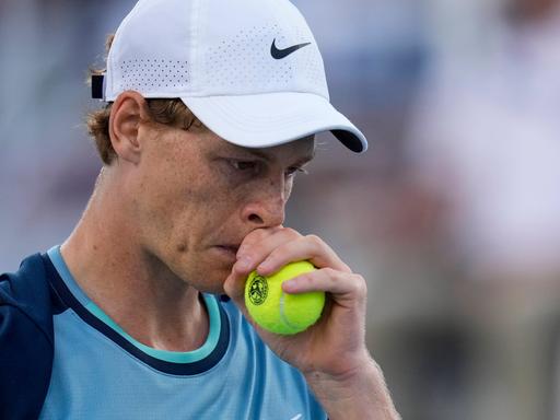 Tennis-Spieler Jannik Sinner in einer Proträt-Aufnahme hält sich einen Tennisball während eines Turnierspiels nachdenkend ans Gesicht.