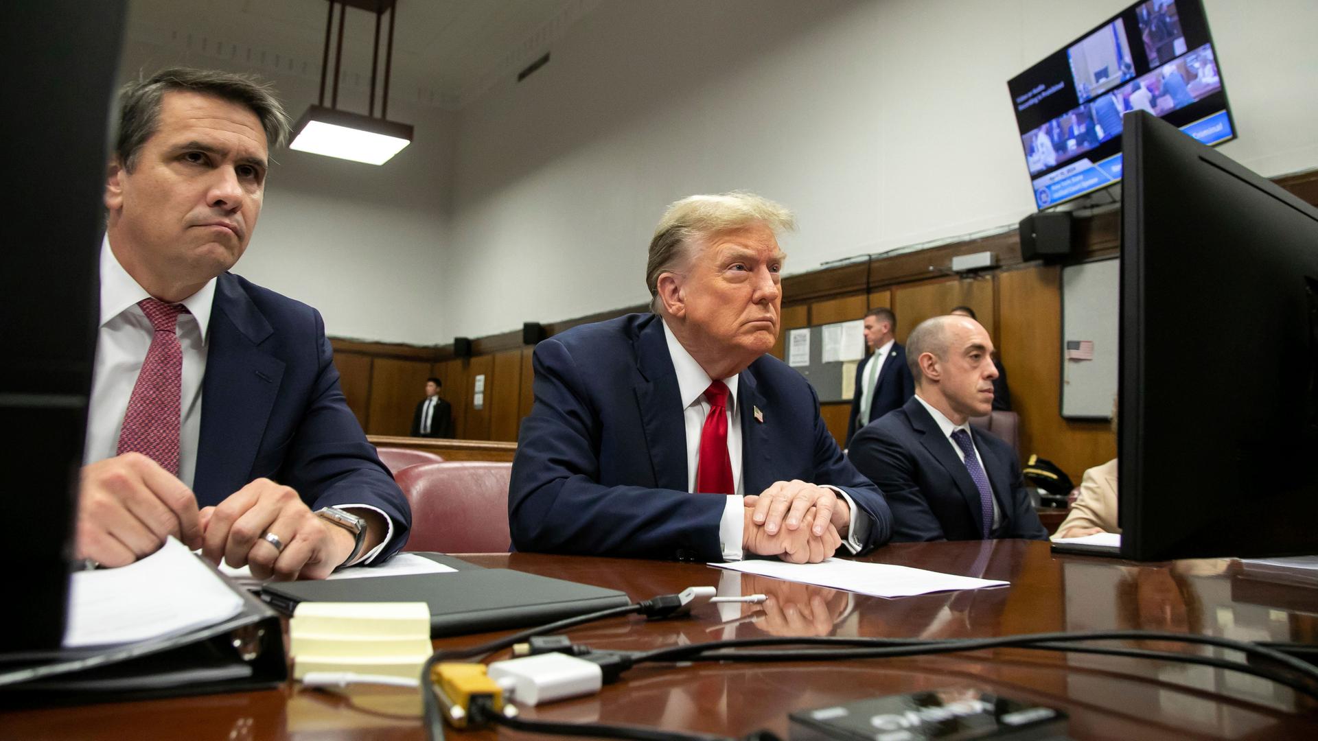 Der frühere US-Präsident Trump sitzt in einem Gericht in New York an einem Tisch. Seine aufeinander gelegten Hände liegen auf einem Blatt Papier.
