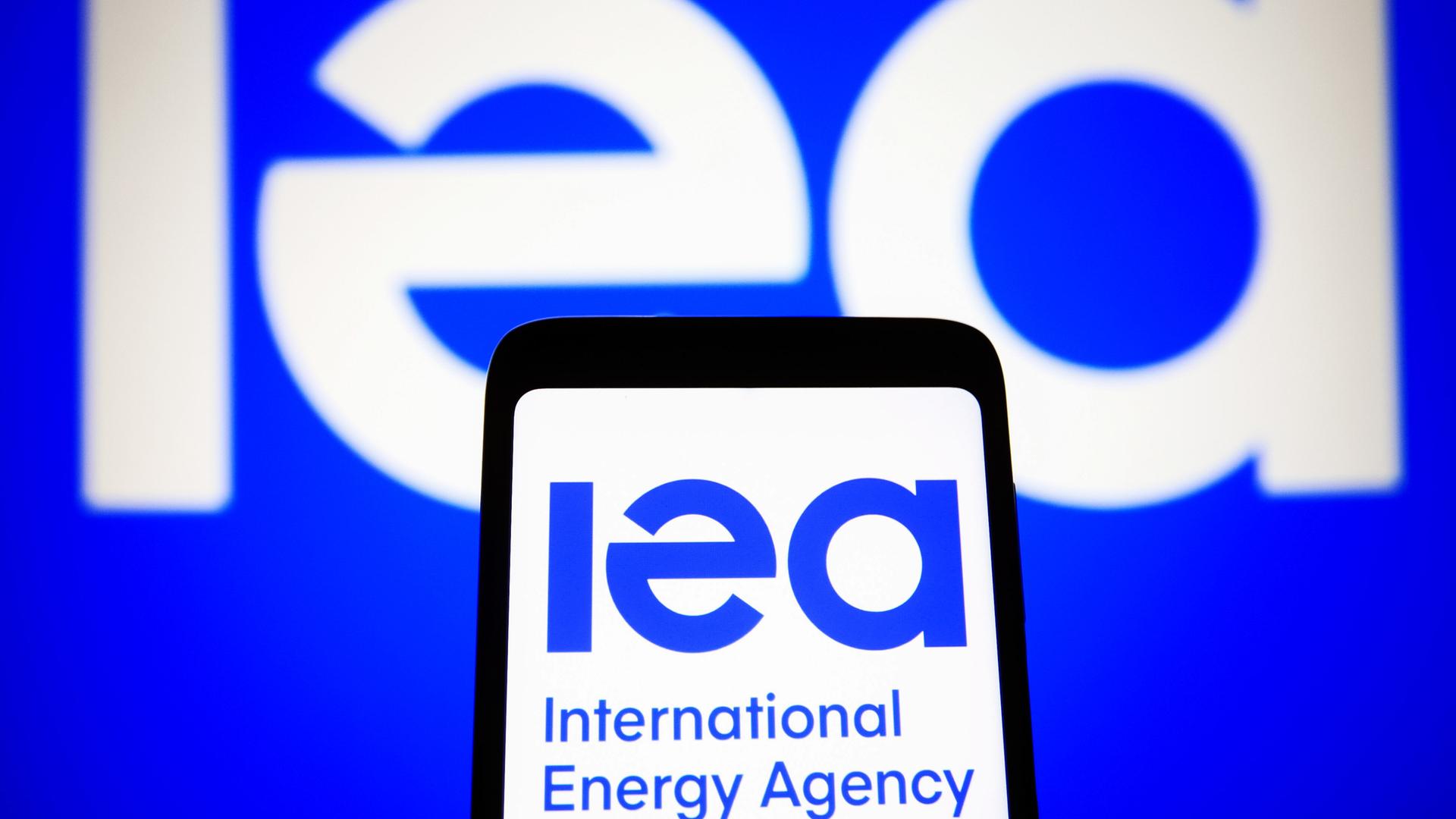 Das IEA-Logo auf einem Handy vor einem großen Logo im Hintergrund