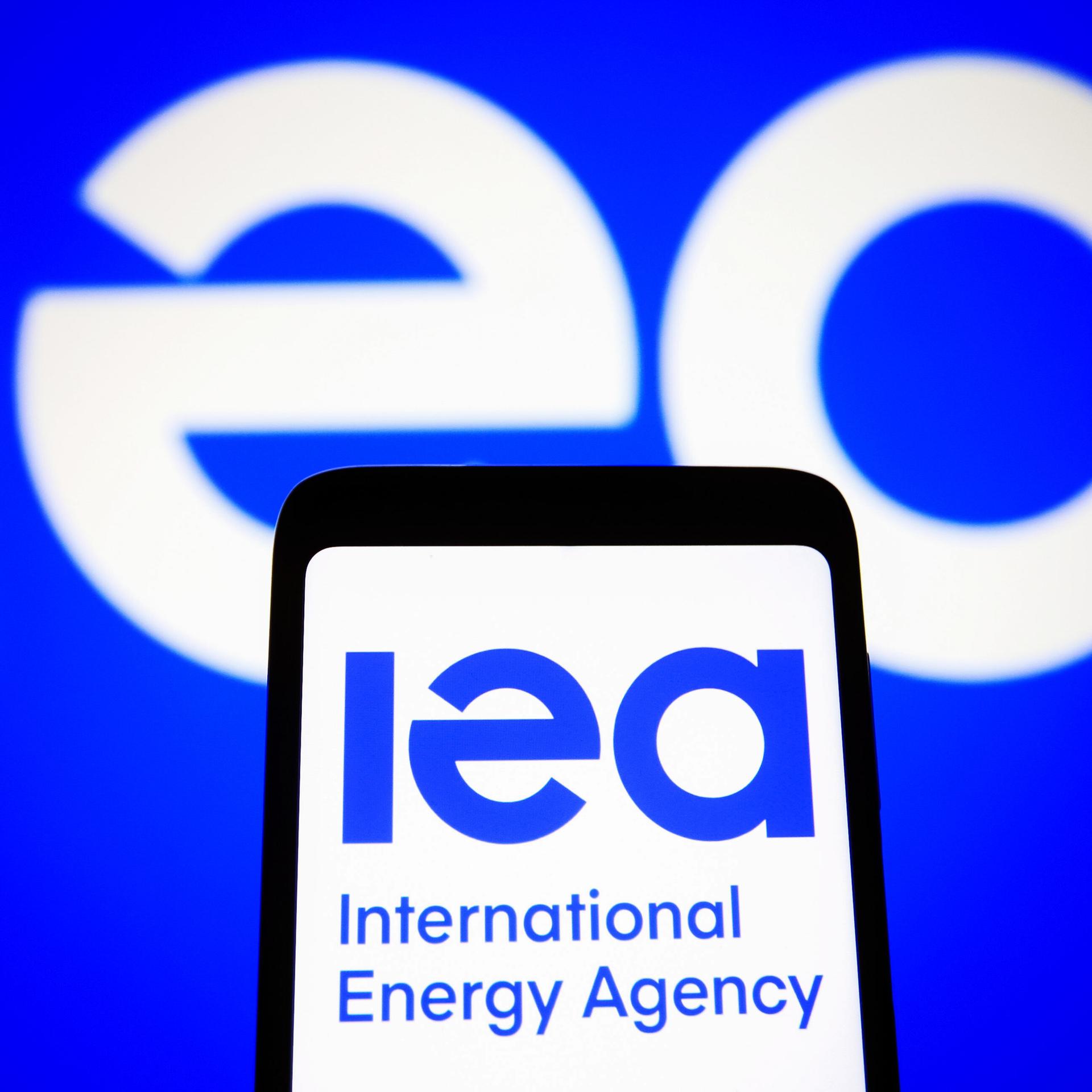 Das IEA-Logo auf einem Handy vor einem großen Logo im Hintergrund