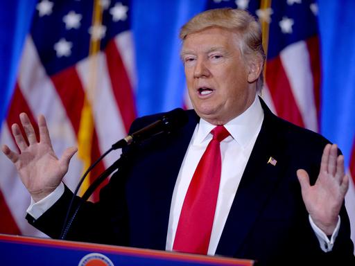 Donald Trump steht hinter einem Rednerpult und streckt die Hände nach oben.