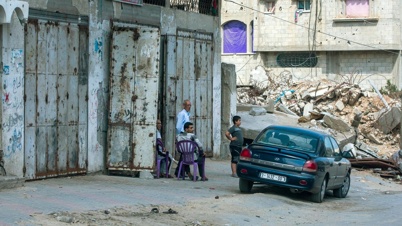 Zerstörte Häuser in Gaza Stadt an einer Zufahrtsstraße zu einem der zerstörten Stadtviertel. Ein Auto und drei Personen stehen daneben. Zerstörte Häuser in Gaza Stadt an einer Zufahrtsstraße zu einem der zerstörten Stadtviertel. Ein Auto und drei Personen stehen daneben.