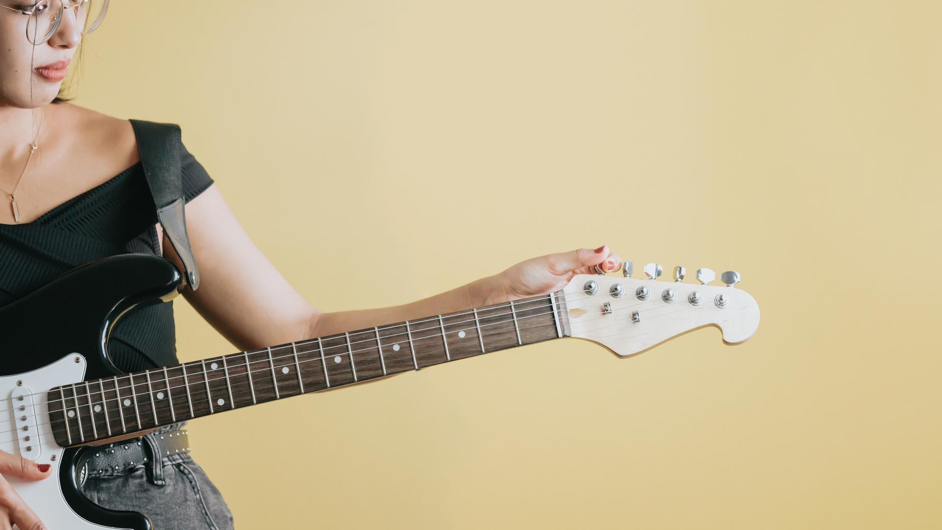 Konzeptuelles Studiobild eines Details einer Frau, die sich bereit macht, eine E-Gitarre zu spielen, gelber Hintergrund, abnehmbarer Hintergrund, Bannerdesign, Werbung in sozialen Netzwerken, Kopierraum