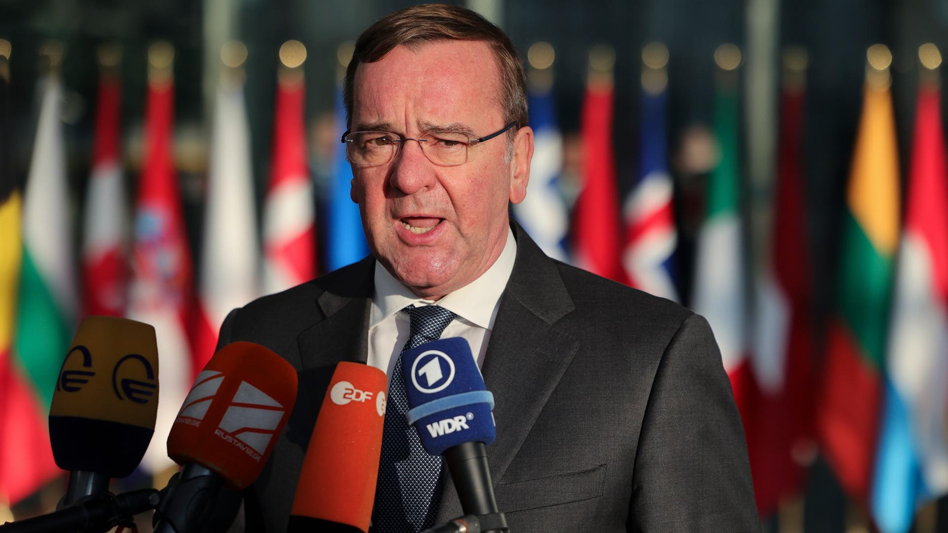 Brüssel: Boris Pistorius, Bundesverteidigungsminister, spricht im Nato-Hauptquartier zu Reportern. Vor ihm Mikrofone, hinter ihm verschwommen die Flaggen der NATO-Länder.